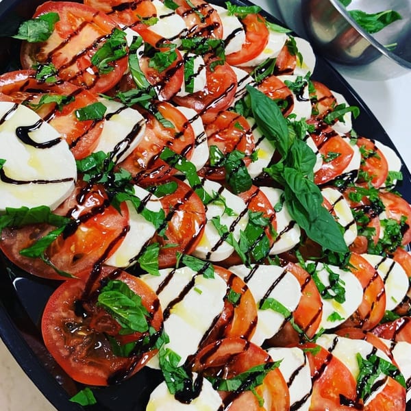 Caprese salad with sliced tomatoes, mozzarella, fresh basil, and balsamic glaze on a black platter.