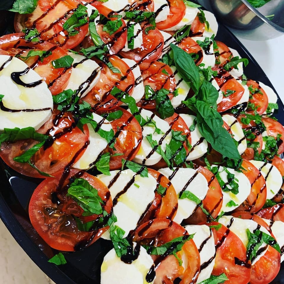Close-up of a large platter of Caprese salad with sliced tomatoes, mozzarella, basil, and balsamic glaze.