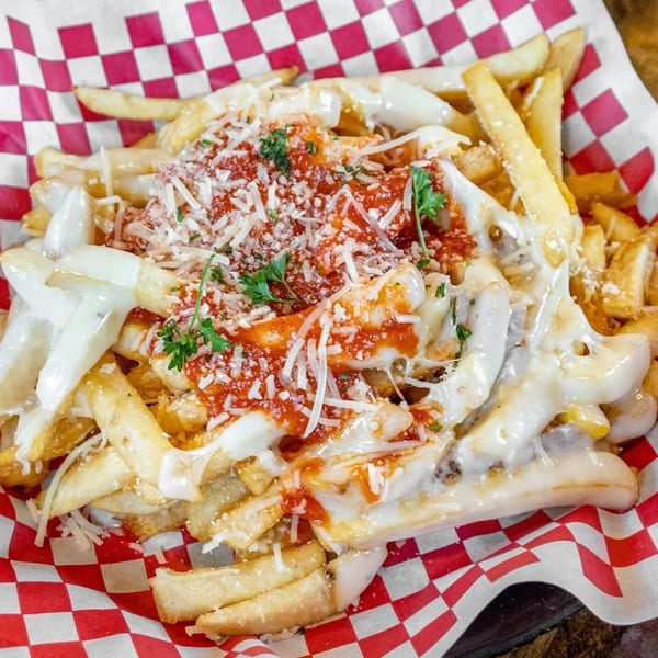 Golden fries topped with melted mozzarella, marinara sauce, Parmesan cheese, and fresh parsley in a red checkered basket.
