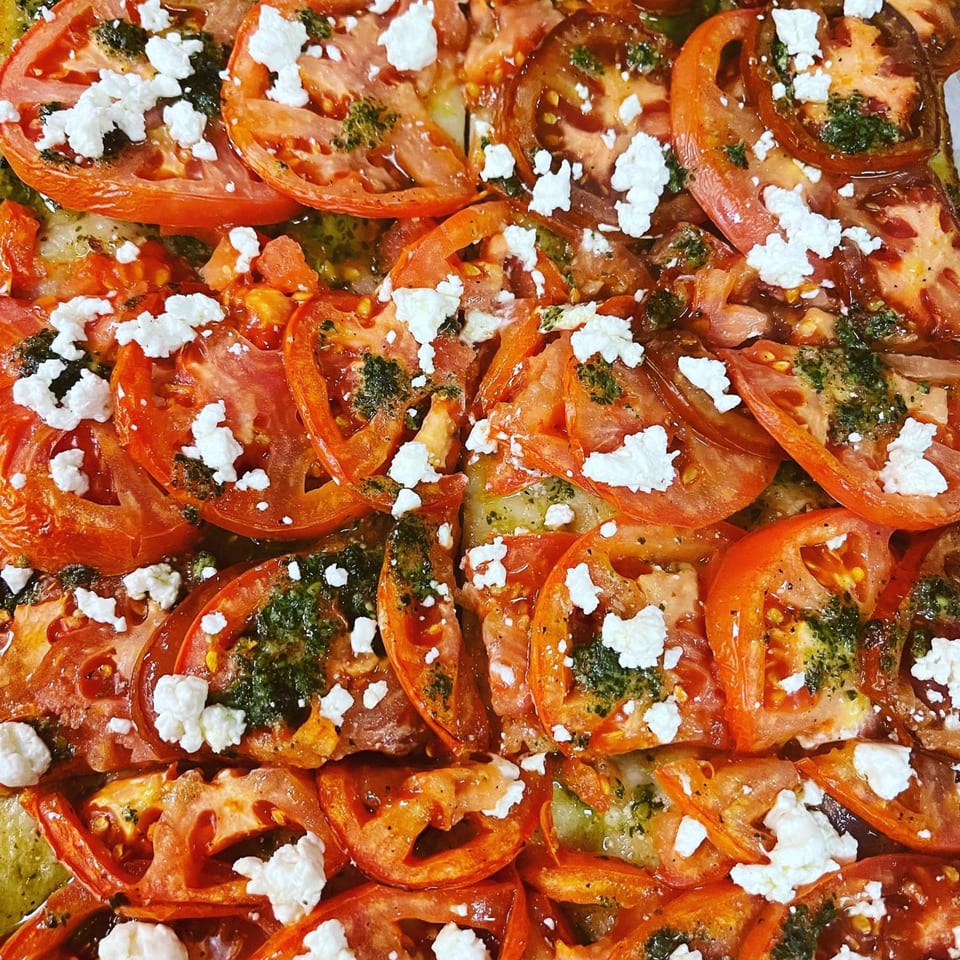 Close-up of a pizza topped with sliced tomatoes, pesto, and crumbled feta cheese.