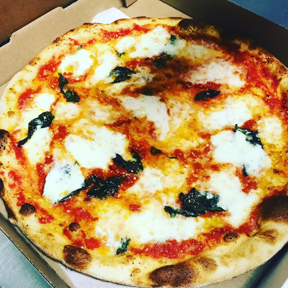A freshly baked Margherita pizza with melted mozzarella, red sauce, and basil in a cardboard box.