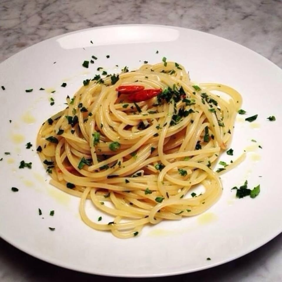 Spaghetti aglio e olio with parsley and red chili pepper on a white plate.