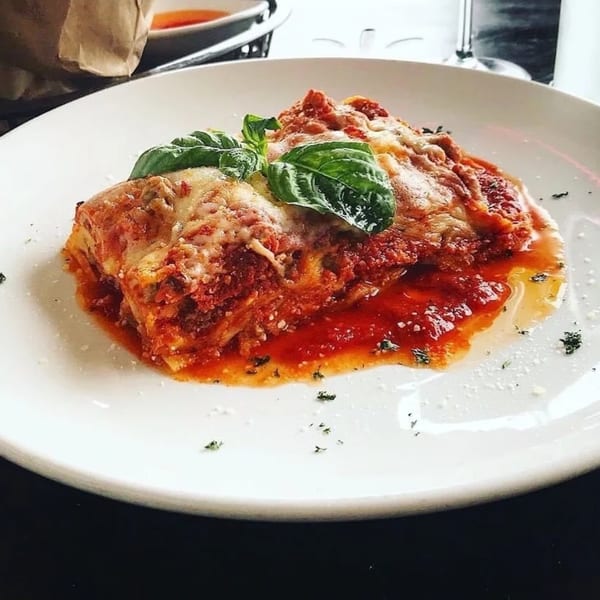 A serving of lasagna with melted cheese, rich red sauce, and fresh basil on a white plate.