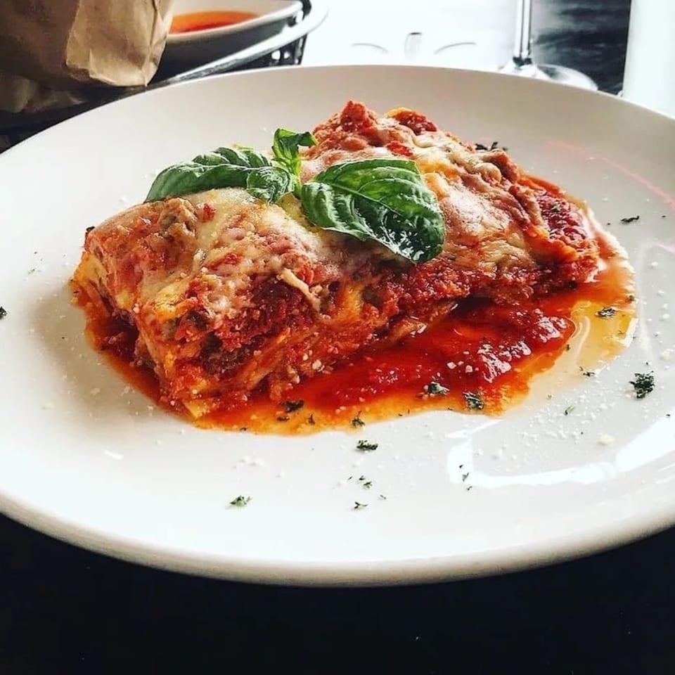 A serving of lasagna with melted cheese, rich red sauce, and fresh basil on a white plate.