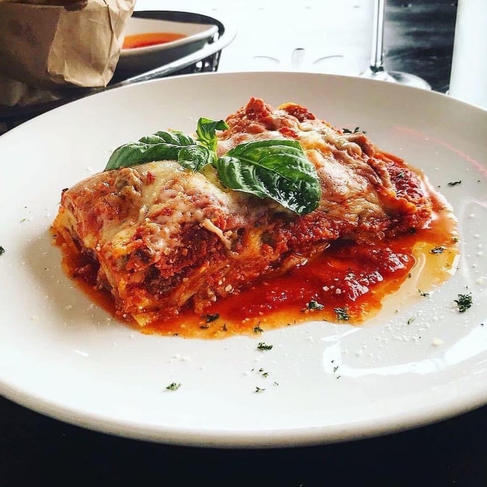 A generous slice of lasagna with melted cheese, rich red sauce, and fresh basil on a white plate.