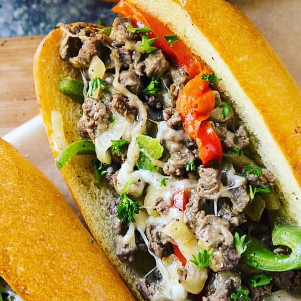 Close-up of a Philly cheesesteak sandwich with steak, melted cheese, peppers, and onions.